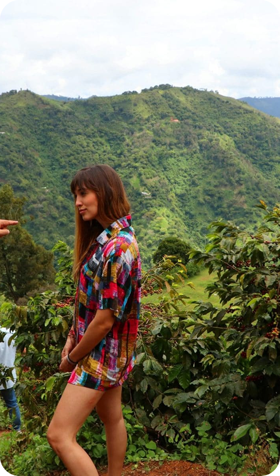 Woman standing in a coffee plantation with green mountains in the background